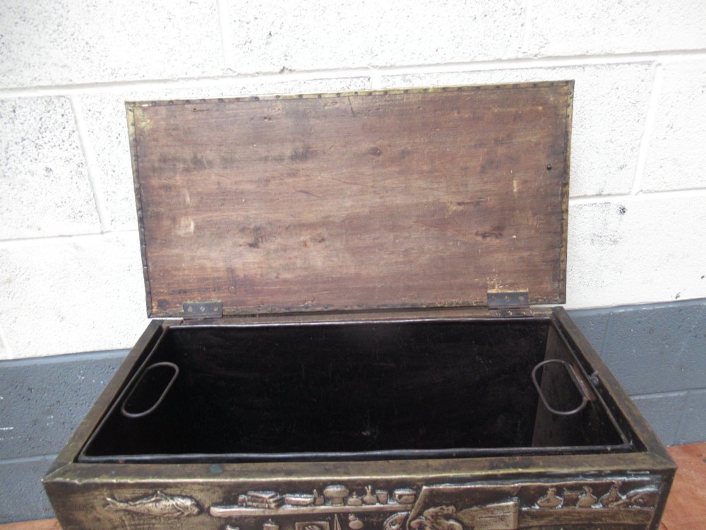 A rectangular Victorian brass log box featuring a detailed embossed relief scene of figures inside a room on the front panel. View VII