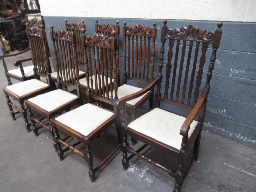 A set of eight 1920s dark oak dining chairs with carved cresting rails, vertical back slats, turned legs, and light cream upholstered seats, including two carvers with armrests. View II
