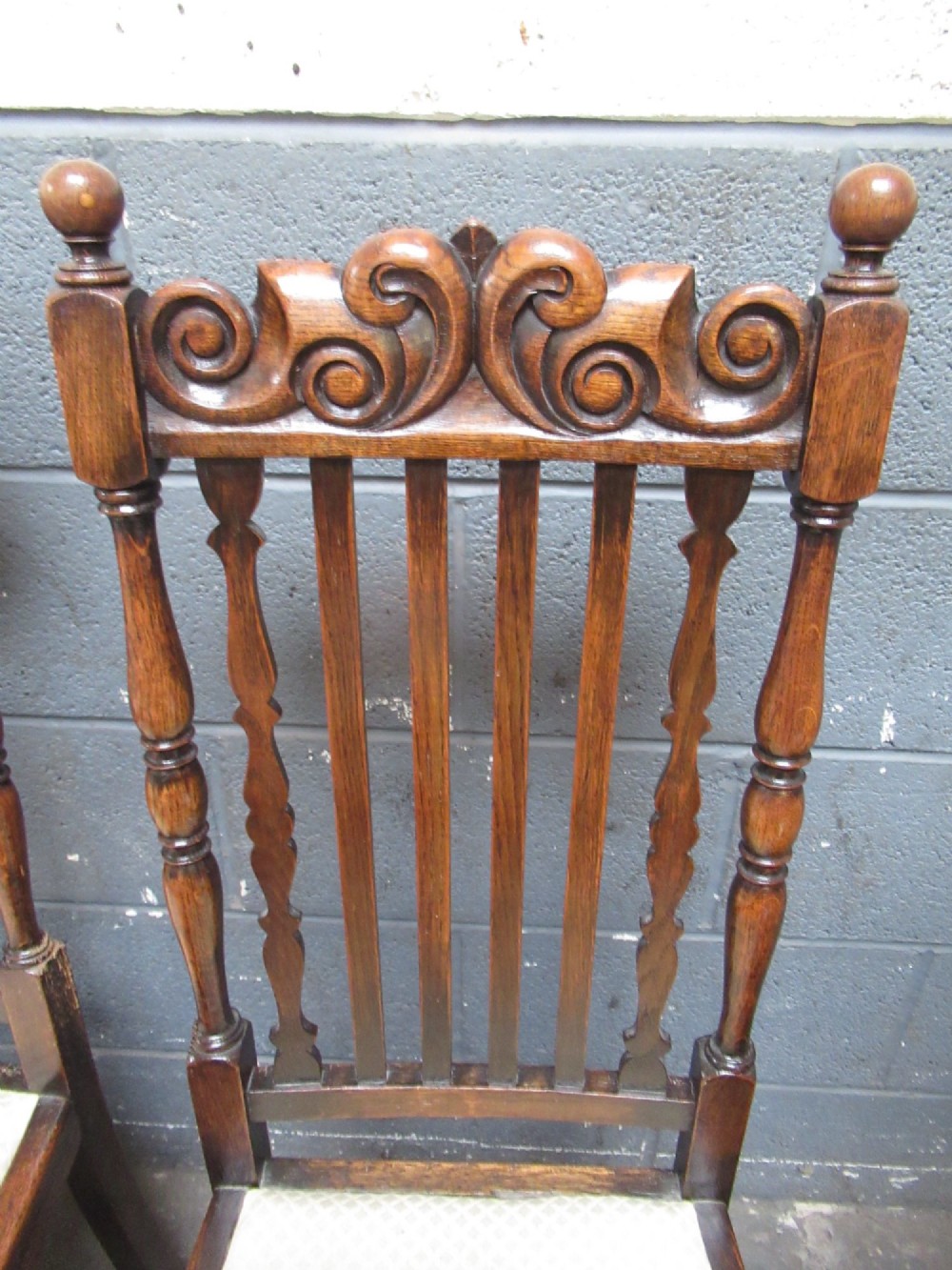A set of eight 1920s dark oak dining chairs with carved cresting rails, vertical back slats, turned legs, and light cream upholstered seats, including two carvers with armrests. View III