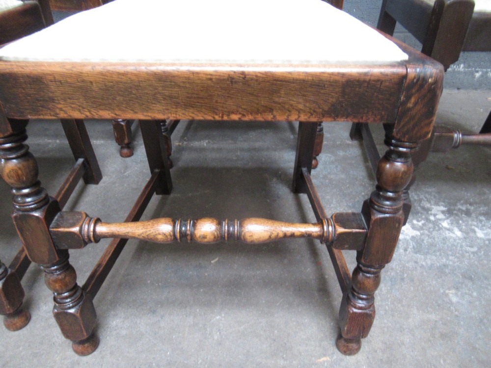 A set of eight 1920s dark oak dining chairs with carved cresting rails, vertical back slats, turned legs, and light cream upholstered seats, including two carvers with armrests. View IV