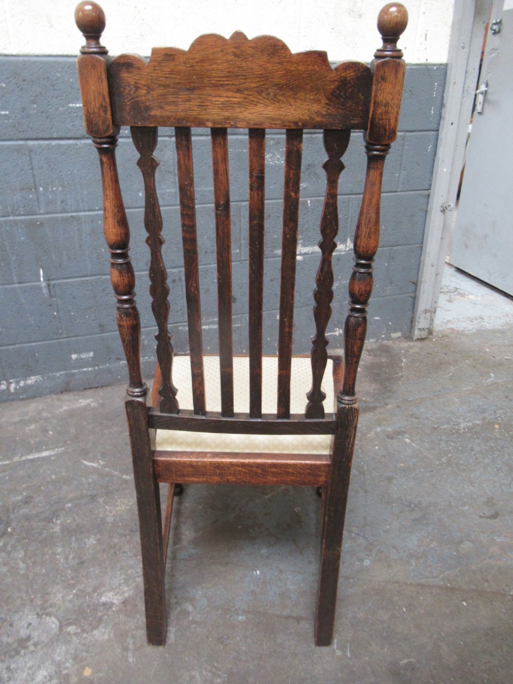 A set of eight 1920s dark oak dining chairs with carved cresting rails, vertical back slats, turned legs, and light cream upholstered seats, including two carvers with armrests. View V