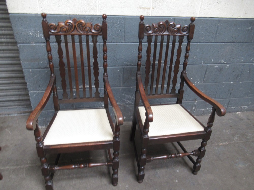 A set of eight 1920s dark oak dining chairs with carved cresting rails, vertical back slats, turned legs, and light cream upholstered seats, including two carvers with armrests. View VI