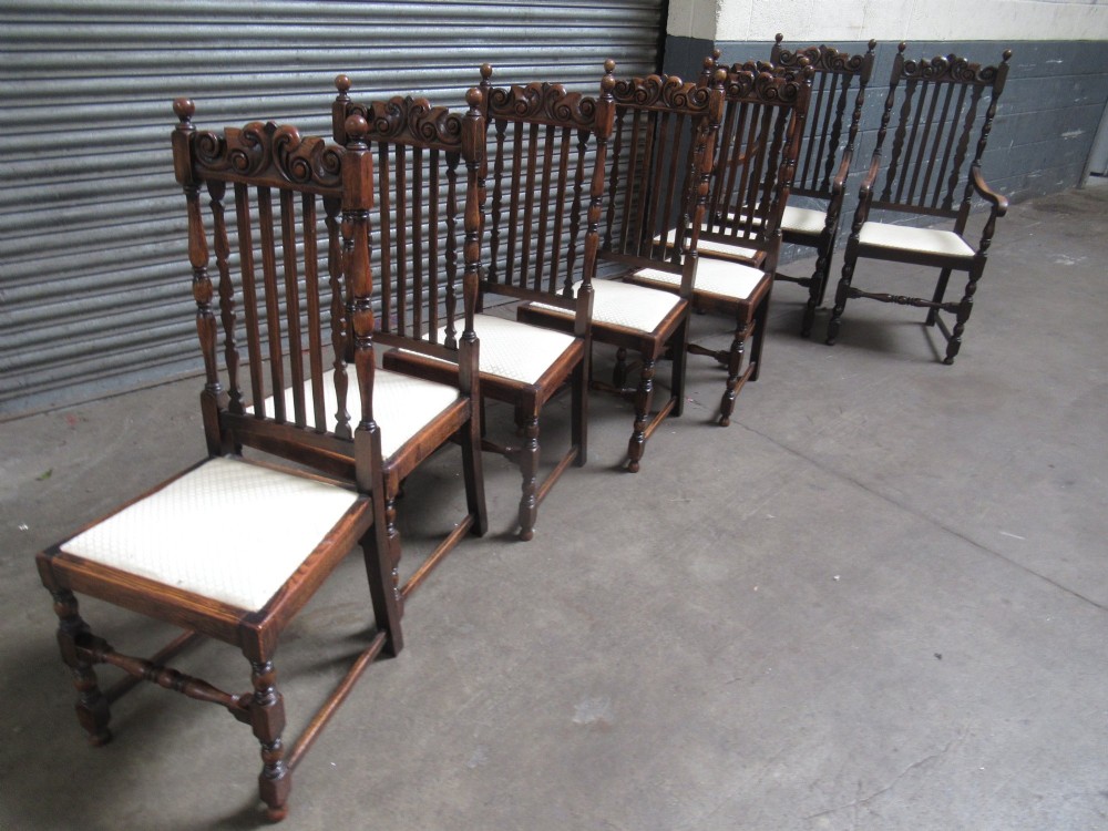 A set of eight 1920s dark oak dining chairs with carved cresting rails, vertical back slats, turned legs, and light cream upholstered seats, including two carvers with armrests. View VIII