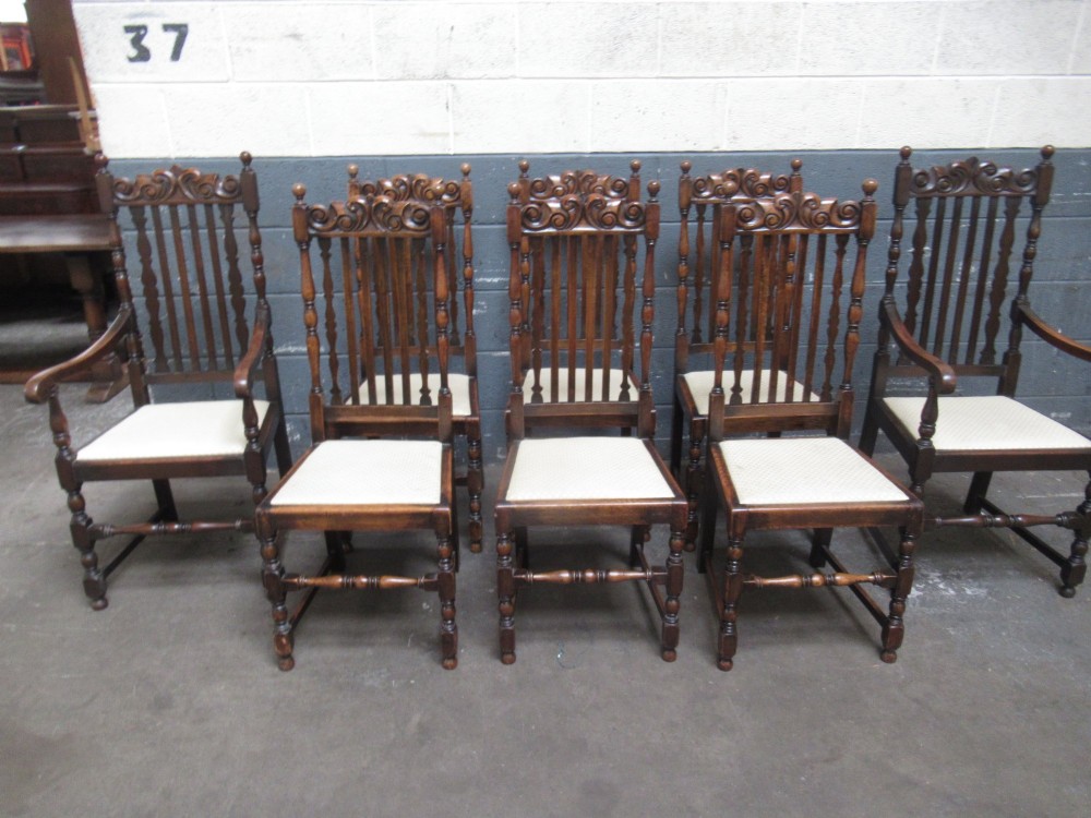 A set of eight 1920s dark oak dining chairs with carved cresting rails, vertical back slats, turned legs, and light cream upholstered seats, including two carvers with armrests. View IX