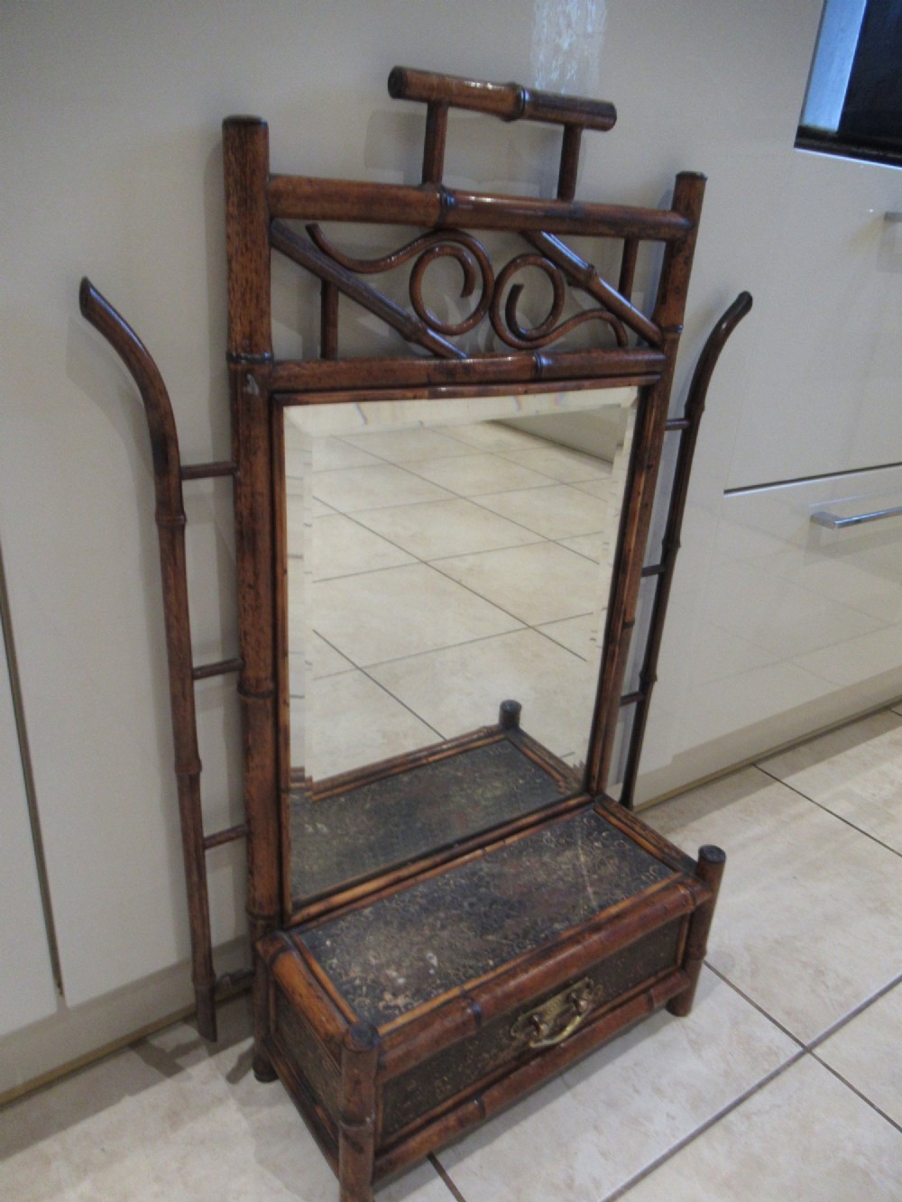 A late Victorian bamboo wall mirror featuring a rectangular bevelled glass plate, bent bamboo scrollwork cresting, side hooks, and a small base drawer with a brass handle.