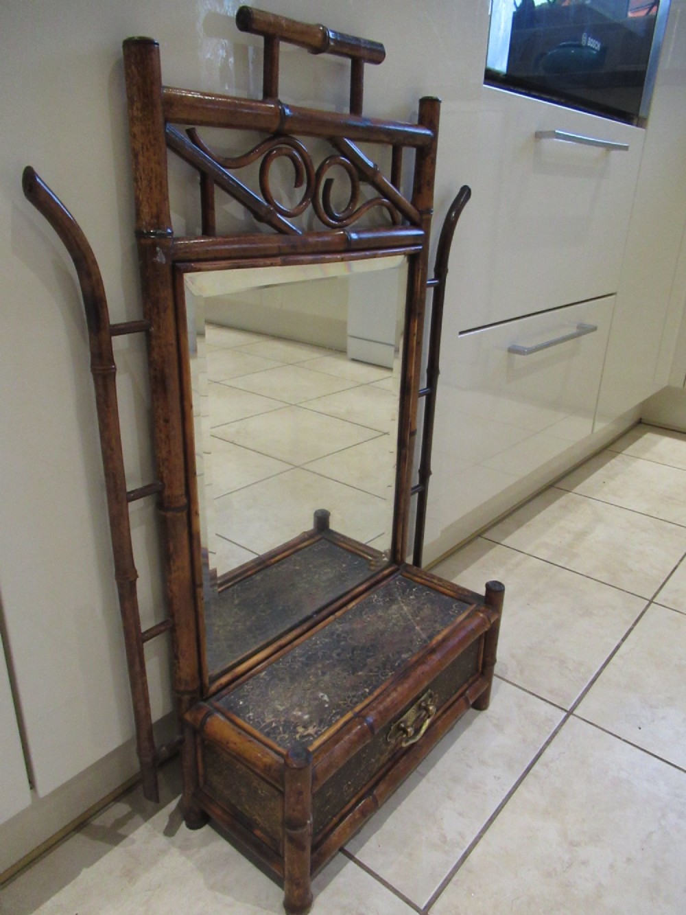 A late Victorian bamboo wall mirror featuring a rectangular bevelled glass plate, bent bamboo scrollwork cresting, side hooks, and a small base drawer with a brass handle. View II