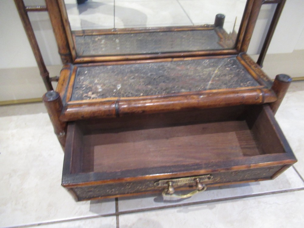 A late Victorian bamboo wall mirror featuring a rectangular bevelled glass plate, bent bamboo scrollwork cresting, side hooks, and a small base drawer with a brass handle. View V