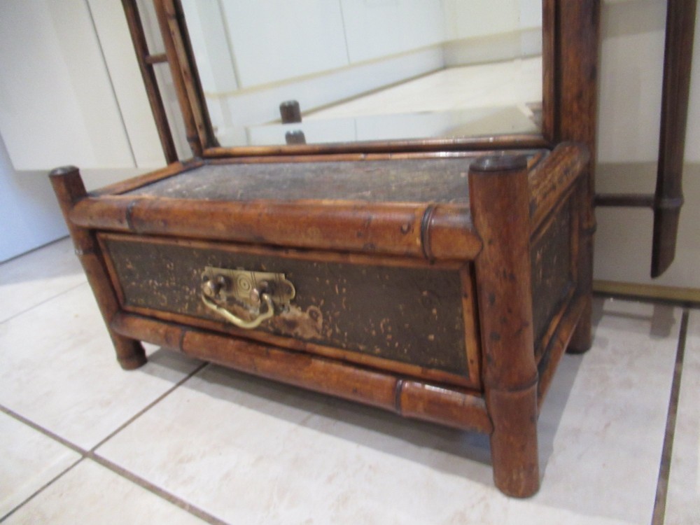 A late Victorian bamboo wall mirror featuring a rectangular bevelled glass plate, bent bamboo scrollwork cresting, side hooks, and a small base drawer with a brass handle. View VI