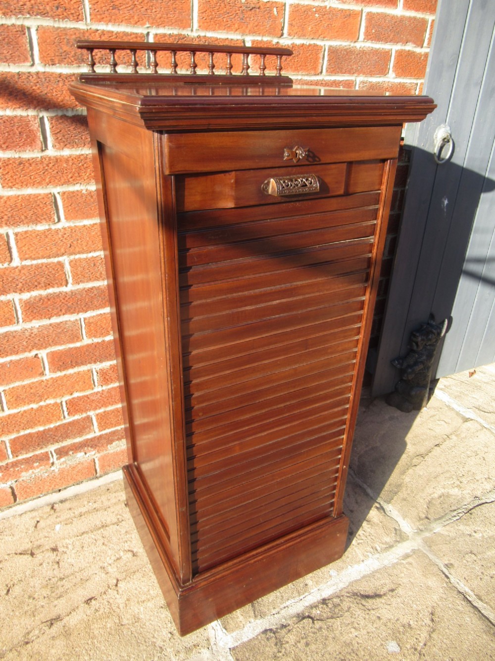 An Edwardian mahogany filing cabinet featuring a slatted tambour roll front door, brass hardware, and a moulded plinth base. View II