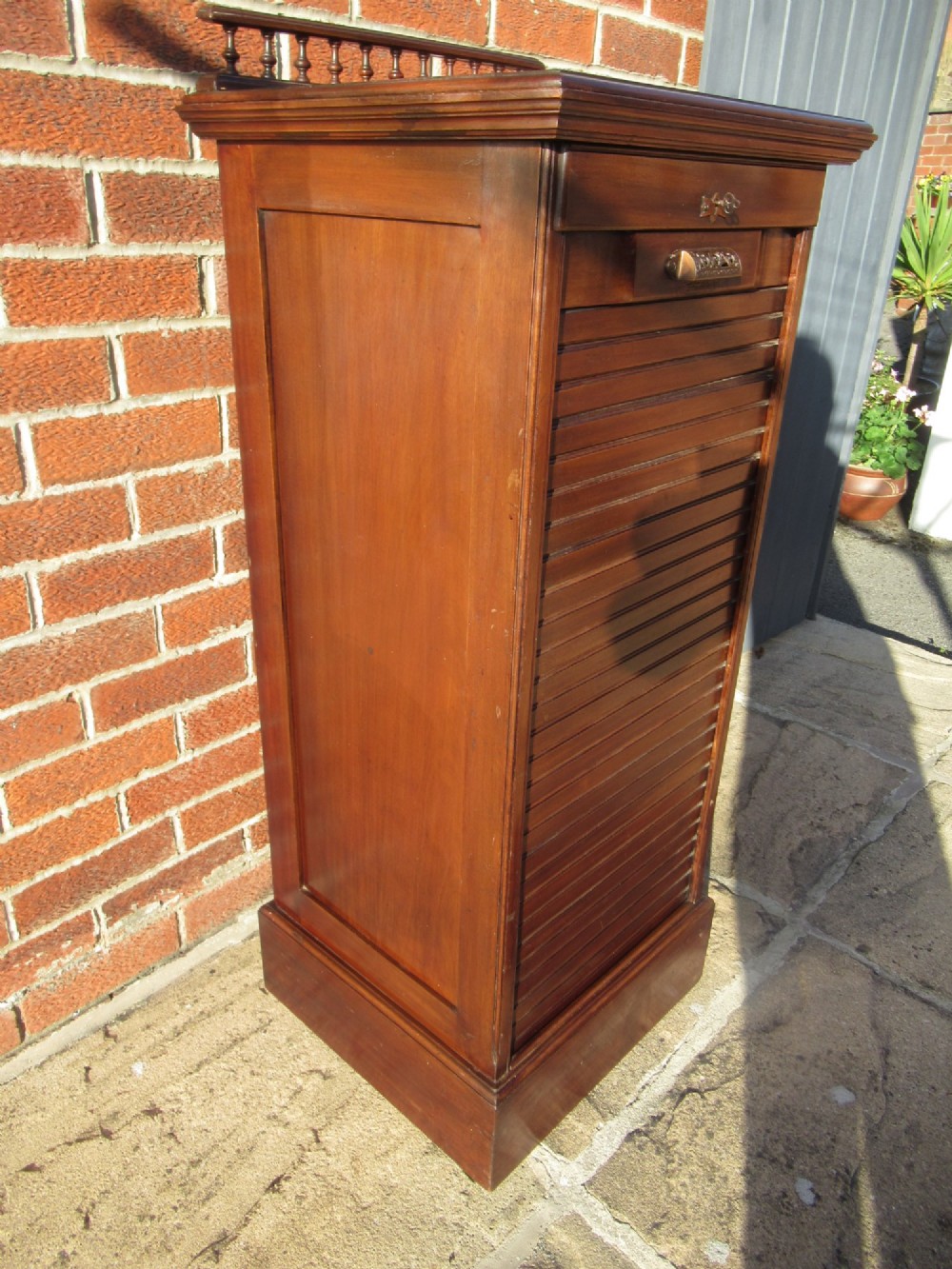 An Edwardian mahogany filing cabinet featuring a slatted tambour roll front door, brass hardware, and a moulded plinth base. View III