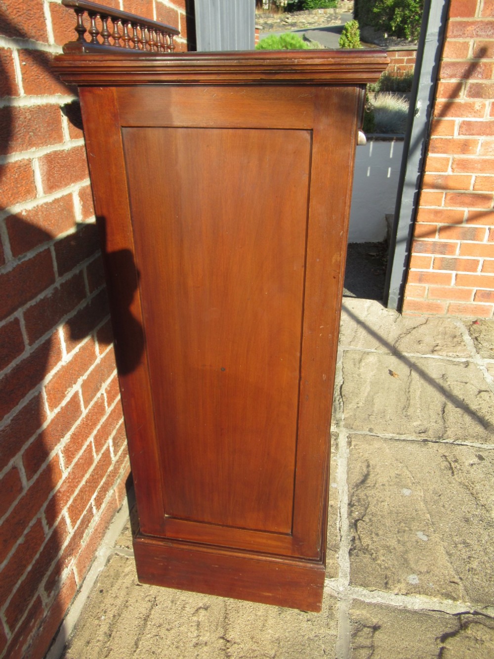 An Edwardian mahogany filing cabinet featuring a slatted tambour roll front door, brass hardware, and a moulded plinth base. View IV