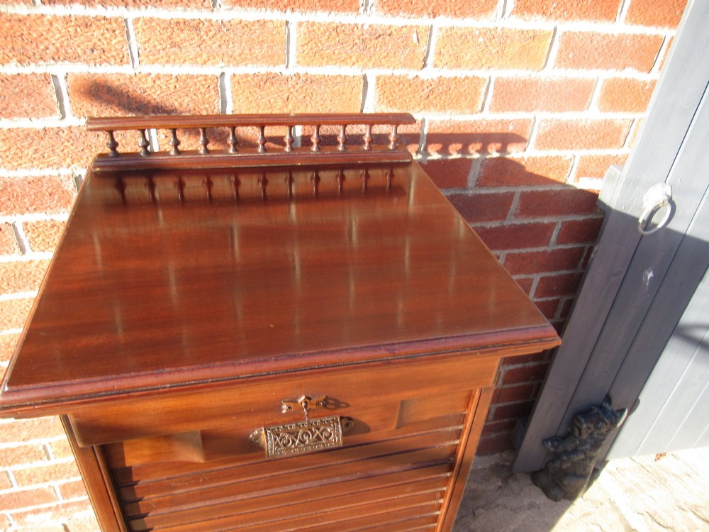 An Edwardian mahogany filing cabinet featuring a slatted tambour roll front door, brass hardware, and a moulded plinth base. View V