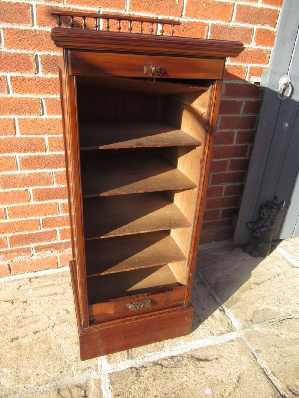 An Edwardian mahogany filing cabinet featuring a slatted tambour roll front door, brass hardware, and a moulded plinth base. View VII