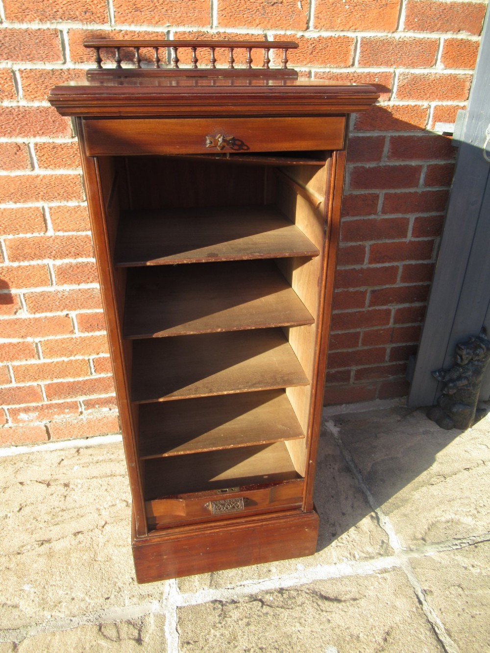 An Edwardian mahogany filing cabinet featuring a slatted tambour roll front door, brass hardware, and a moulded plinth base. View VIII