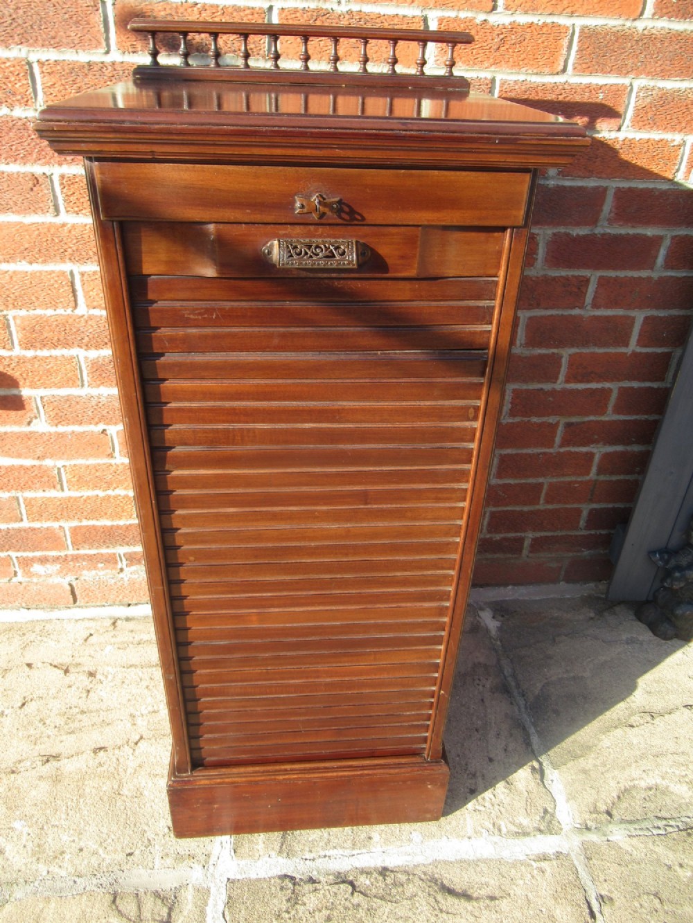 An Edwardian mahogany filing cabinet featuring a slatted tambour roll front door, brass hardware, and a moulded plinth base. View X