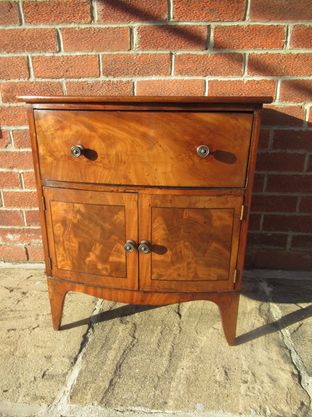A bowfront Victorian mahogany side cabinet featuring a top drawer and two cupboard doors with flame veneer panels.