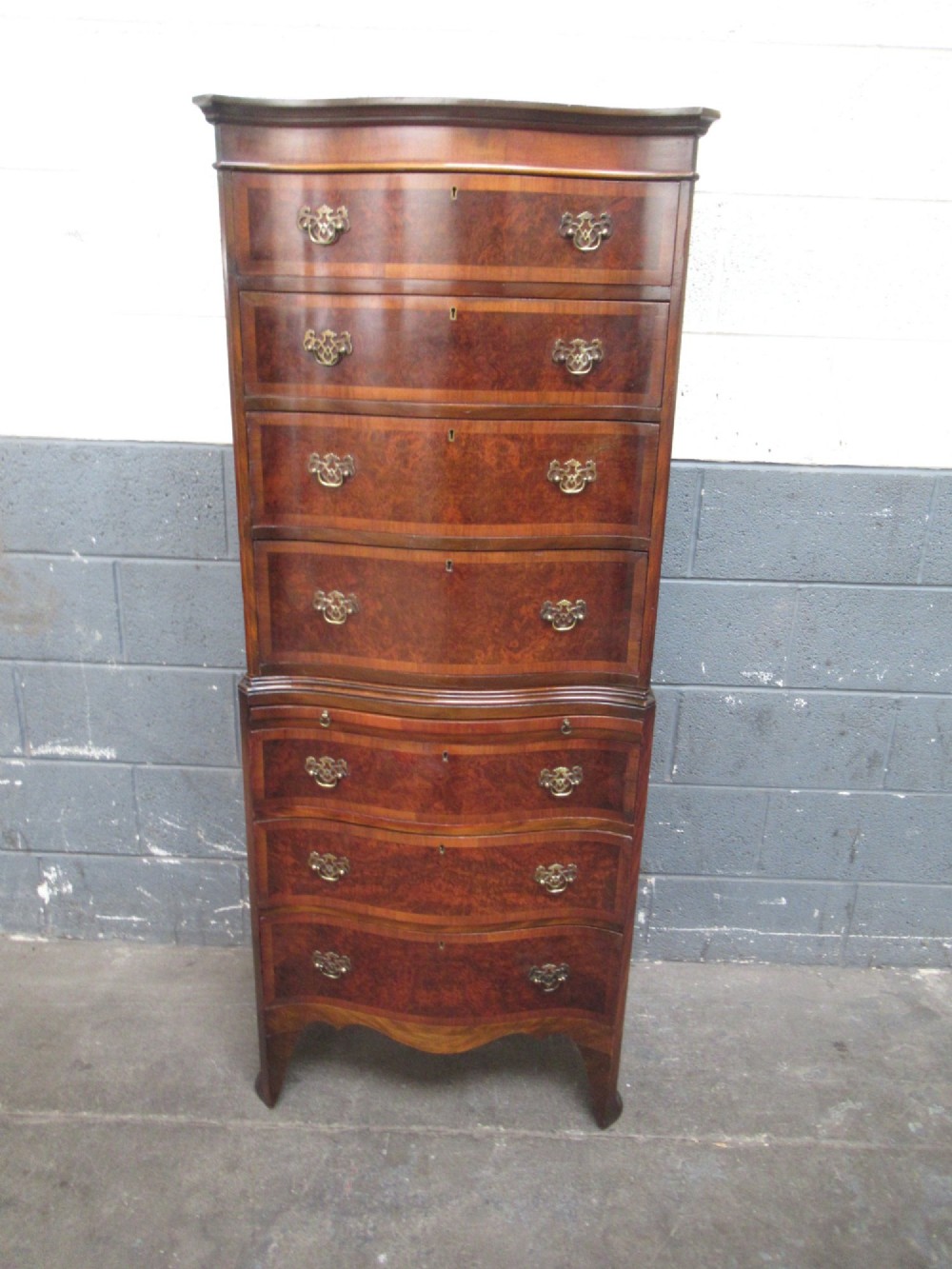 A tall, slim burr walnut chest on chest with a serpentine front, featuring multiple graduated drawers with decorative brass drop handles. View II