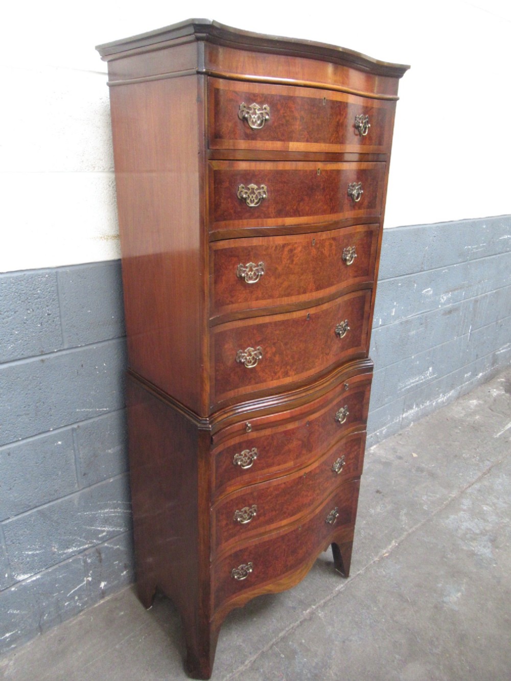 A tall, slim burr walnut chest on chest with a serpentine front, featuring multiple graduated drawers with decorative brass drop handles. View III