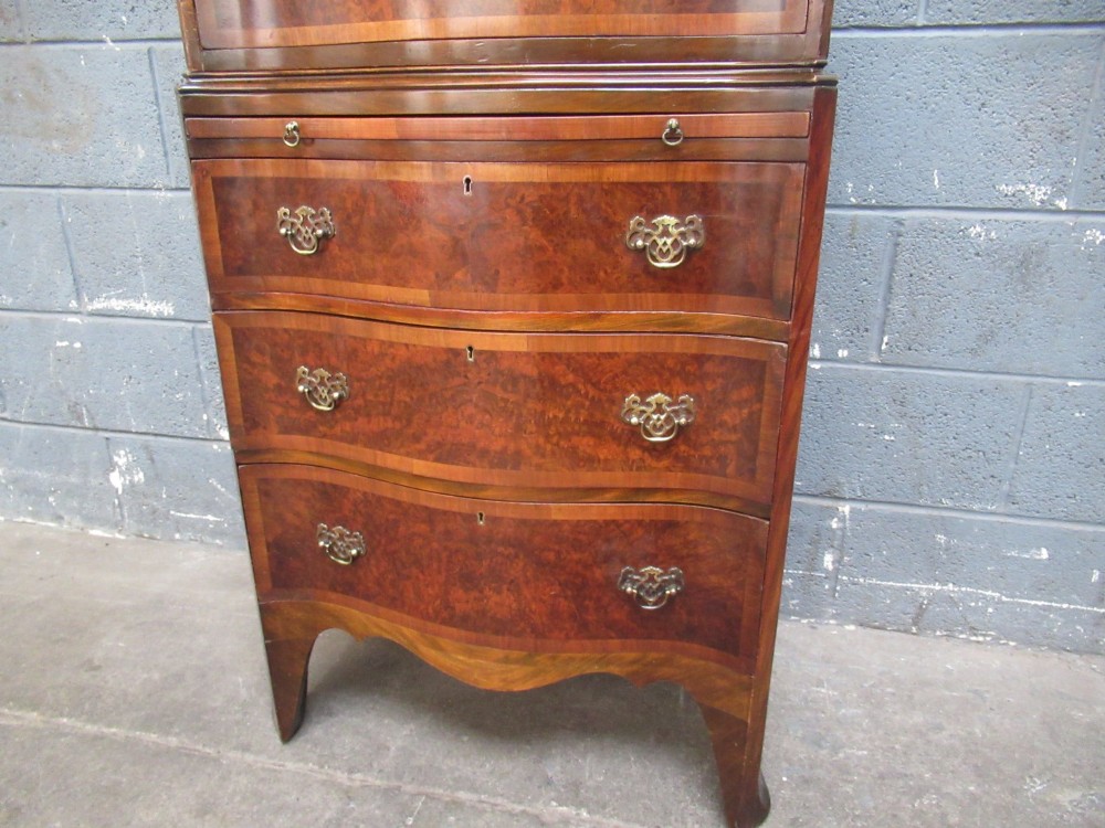 A tall, slim burr walnut chest on chest with a serpentine front, featuring multiple graduated drawers with decorative brass drop handles. View VI