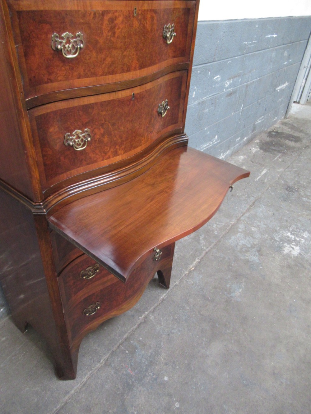 A tall, slim burr walnut chest on chest with a serpentine front, featuring multiple graduated drawers with decorative brass drop handles. View VII