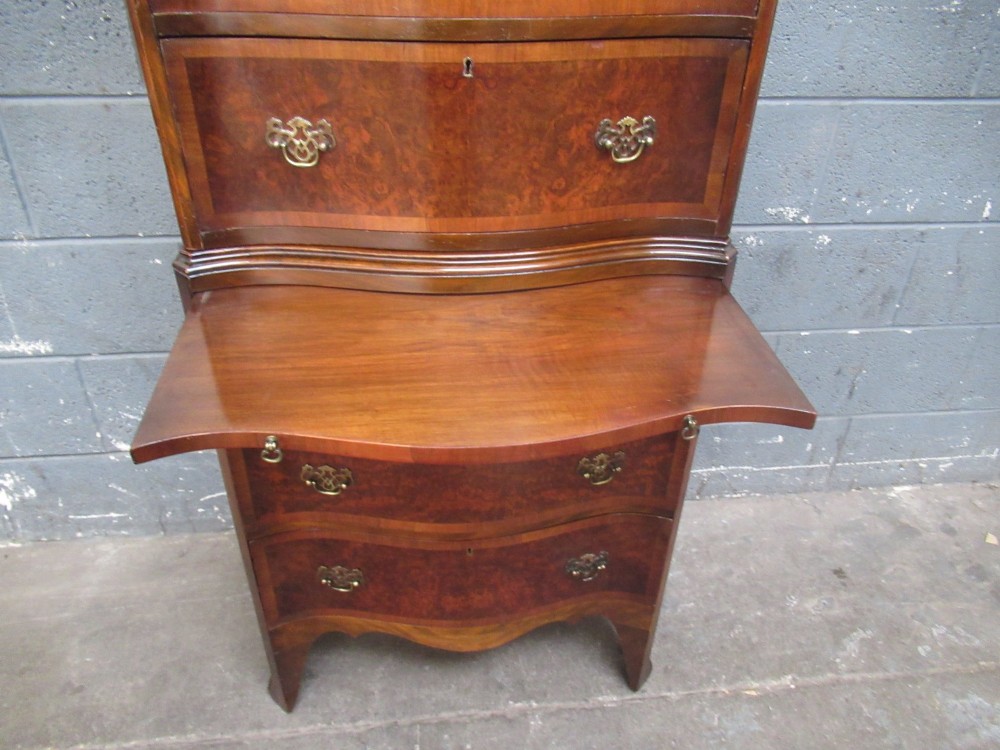 A tall, slim burr walnut chest on chest with a serpentine front, featuring multiple graduated drawers with decorative brass drop handles. View VIII