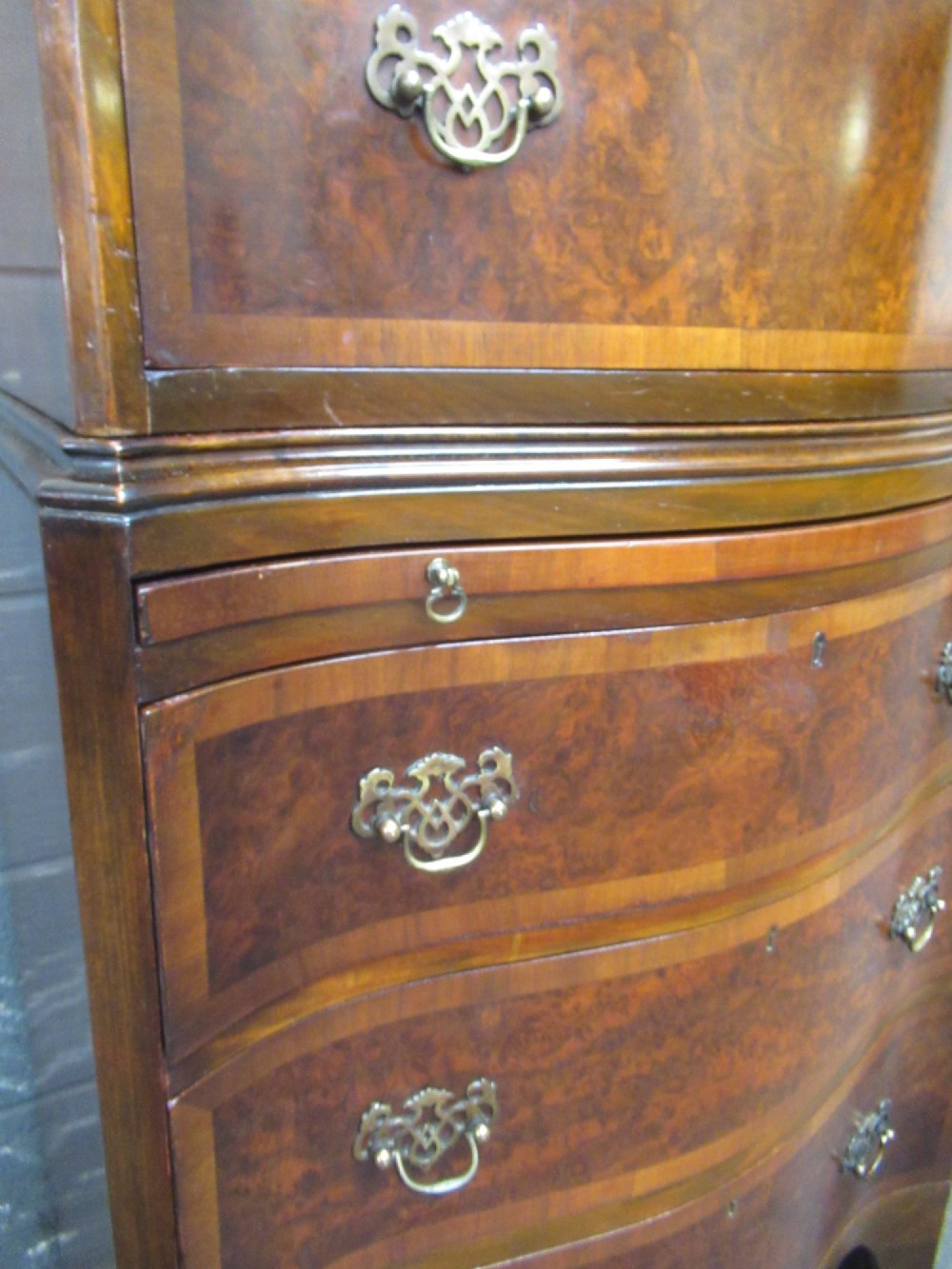 A tall, slim burr walnut chest on chest with a serpentine front, featuring multiple graduated drawers with decorative brass drop handles. View X