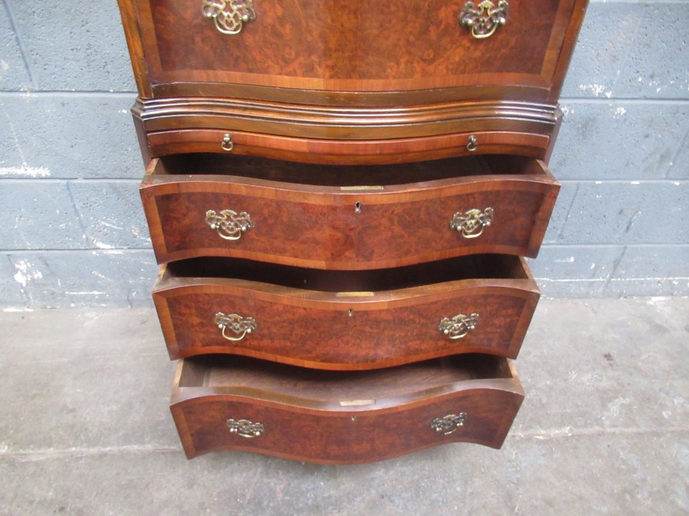 A tall, slim burr walnut chest on chest with a serpentine front, featuring multiple graduated drawers with decorative brass drop handles. View XI