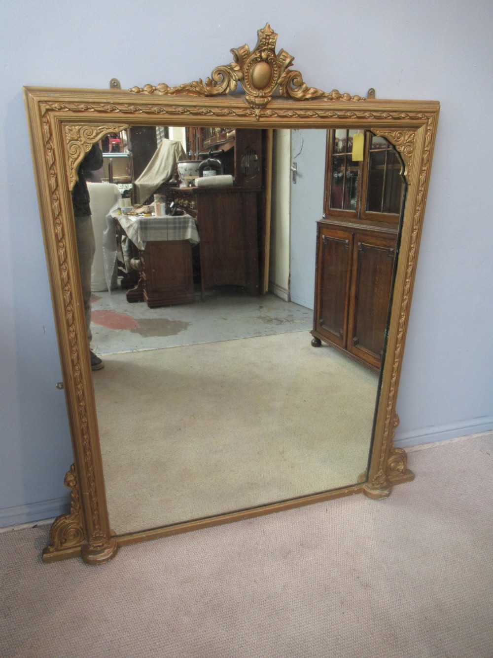 A large rectangular Victorian gilt plaster overmantel mirror featuring an ornate central crest and decorative corner spandrels.