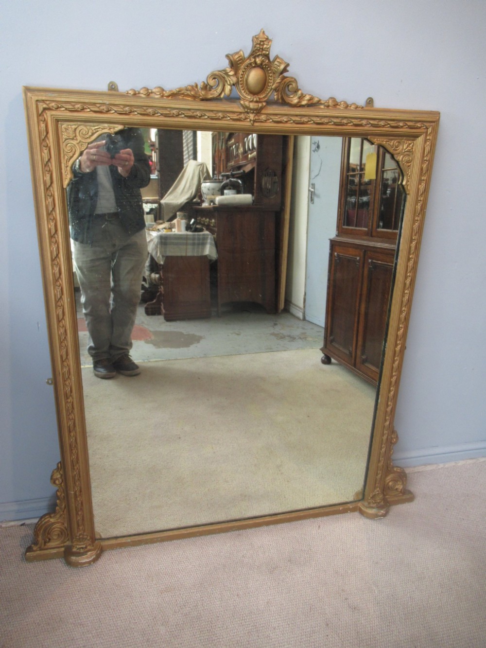 A large rectangular Victorian gilt plaster overmantel mirror featuring an ornate central crest and decorative corner spandrels. View II