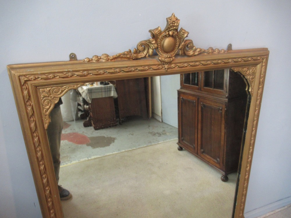 A large rectangular Victorian gilt plaster overmantel mirror featuring an ornate central crest and decorative corner spandrels. View III