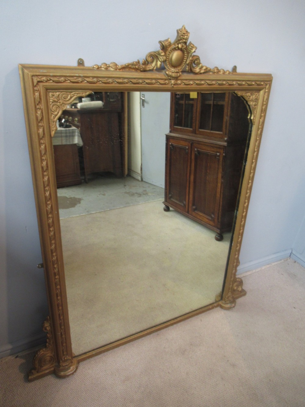 A large rectangular Victorian gilt plaster overmantel mirror featuring an ornate central crest and decorative corner spandrels. View VI