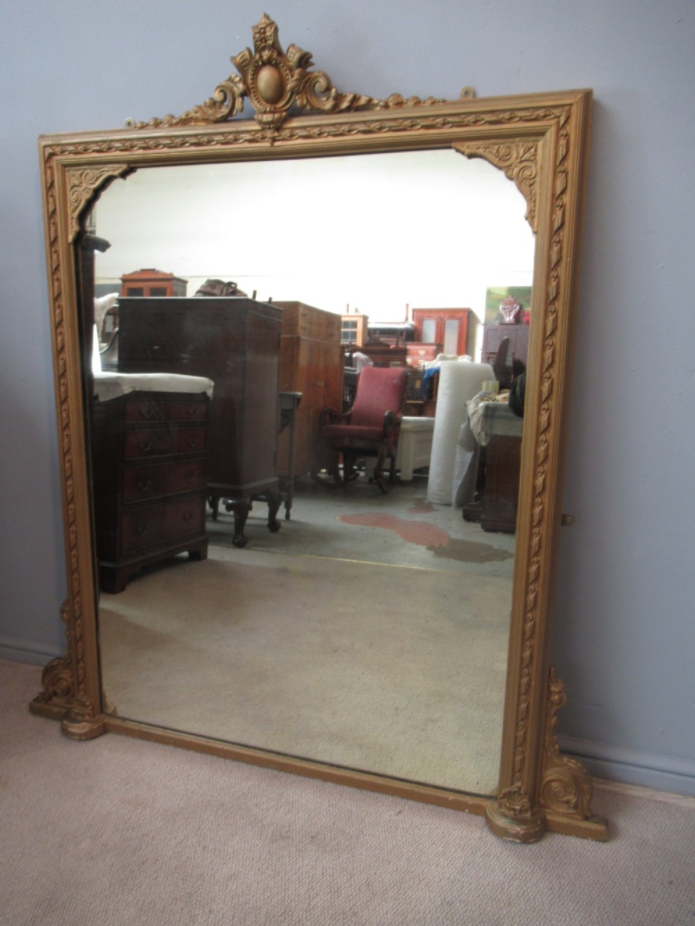 A large rectangular Victorian gilt plaster overmantel mirror featuring an ornate central crest and decorative corner spandrels. View VII