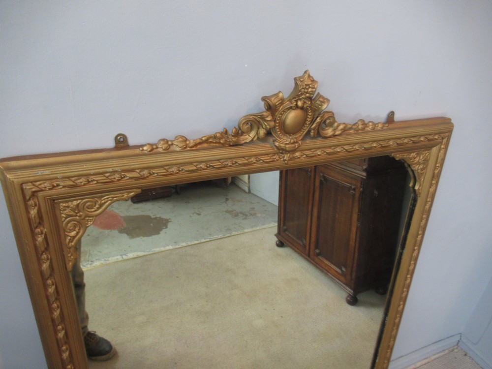 A large rectangular Victorian gilt plaster overmantel mirror featuring an ornate central crest and decorative corner spandrels. View VIII