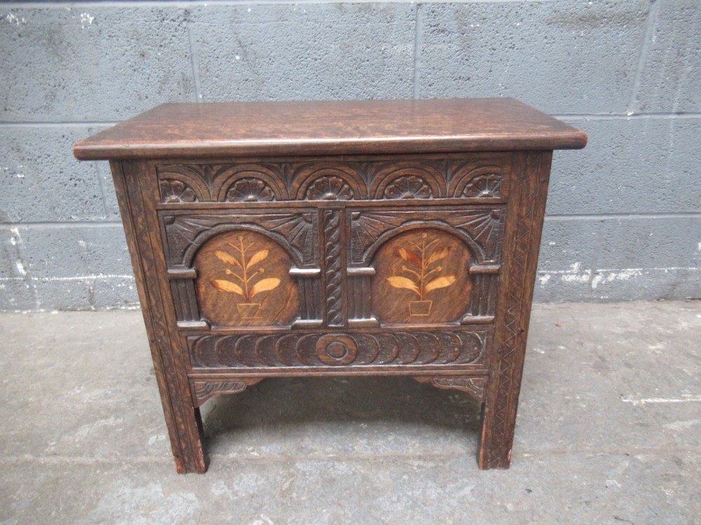 A small dark carved oak coffer featuring two inlaid floral panels, carved arches, and a flat top lid.