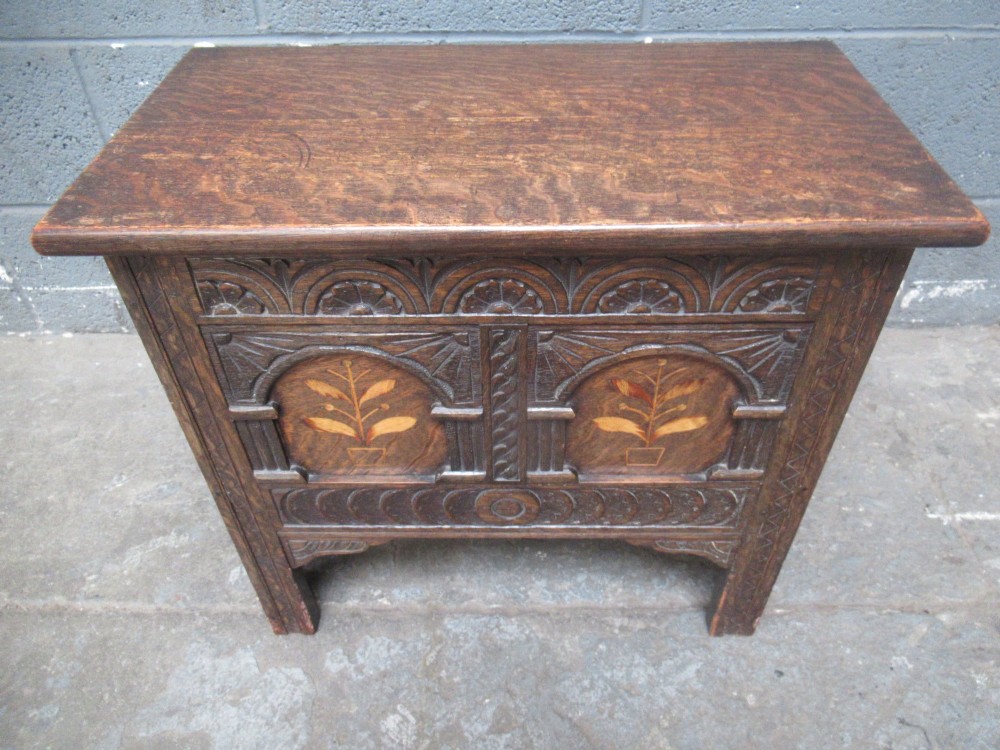 A small dark carved oak coffer featuring two inlaid floral panels, carved arches, and a flat top lid. View II