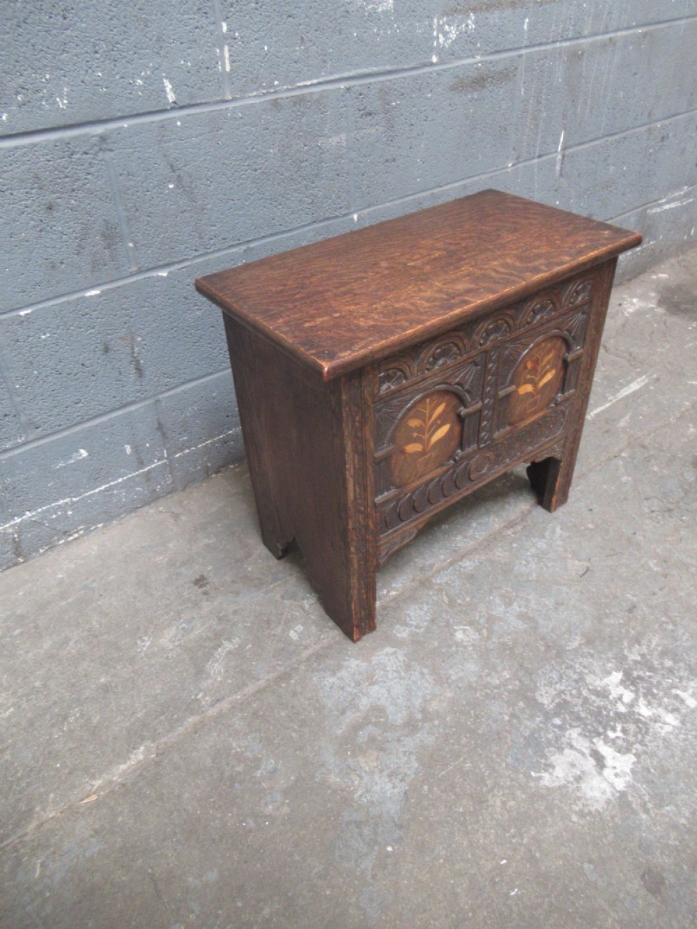 A small dark carved oak coffer featuring two inlaid floral panels, carved arches, and a flat top lid. View IV
