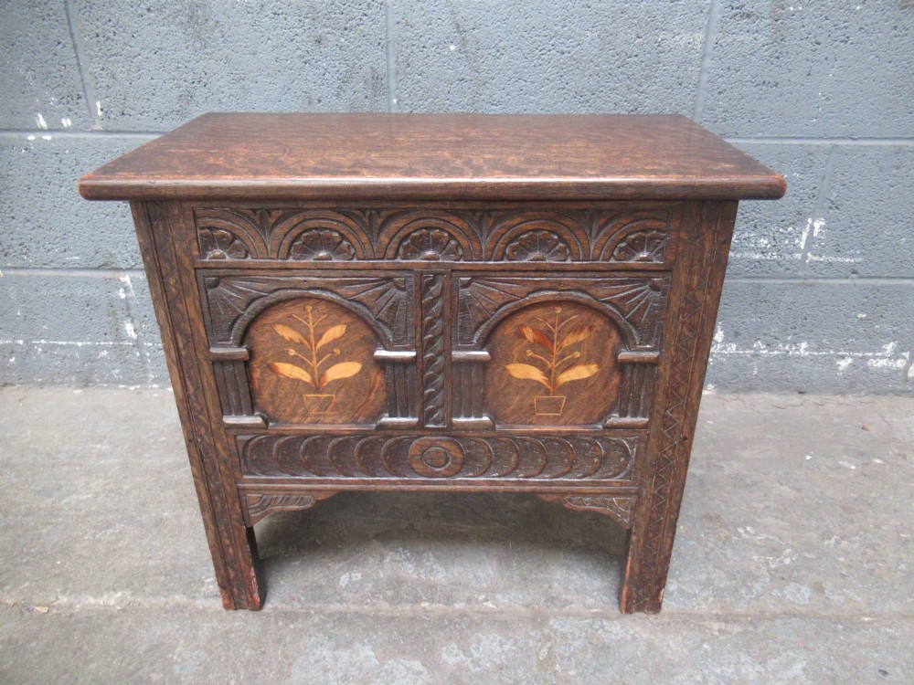 A small dark carved oak coffer featuring two inlaid floral panels, carved arches, and a flat top lid. View IX