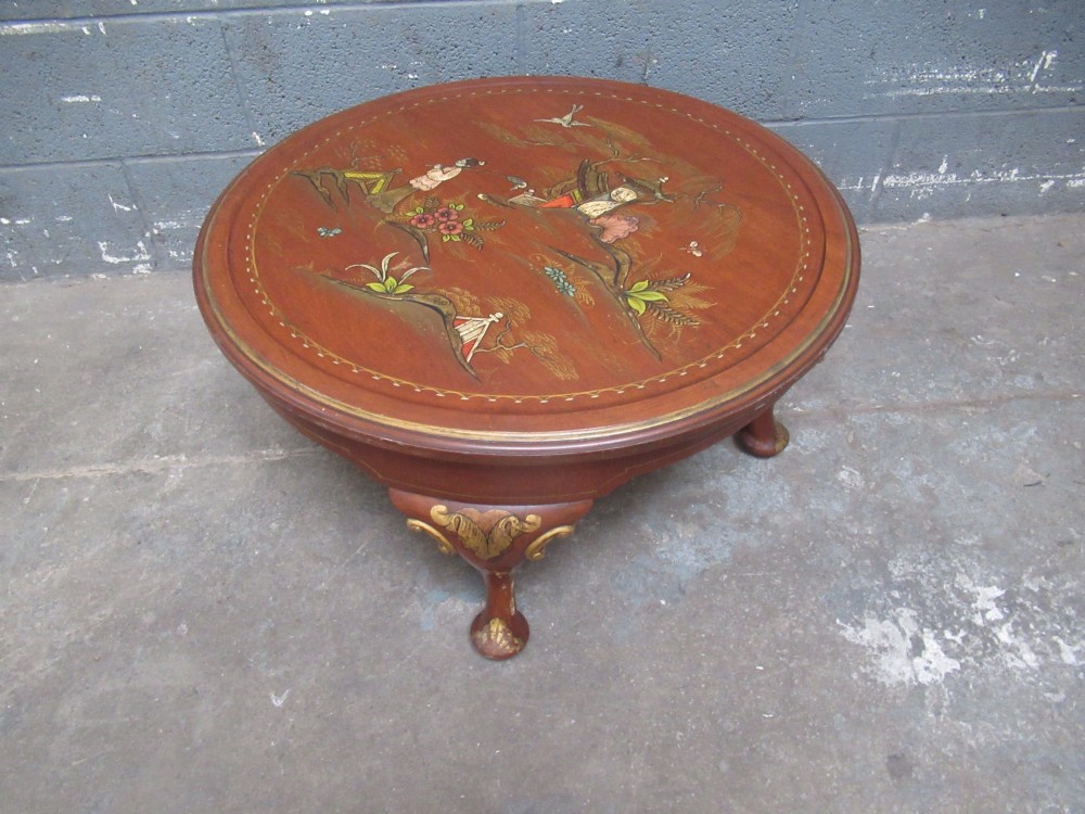 A circular 1930s Chinoiserie coffee table featuring hand-painted oriental figures and flora on a terracotta red lacquered top with gilt-decorated cabriole legs.
