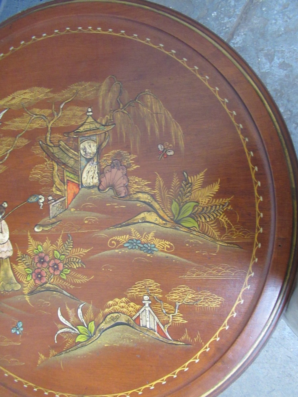 A circular 1930s Chinoiserie coffee table featuring hand-painted oriental figures and flora on a terracotta red lacquered top with gilt-decorated cabriole legs. View IV