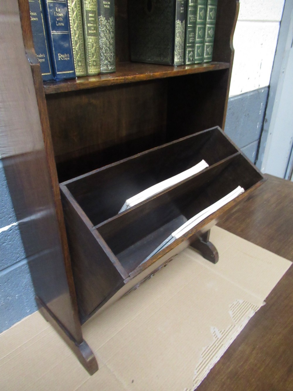 A 1930s dark oak freestanding book rack and magazine holder featuring open shelving above a partitioned lower trough with a carved shell motif. View III
