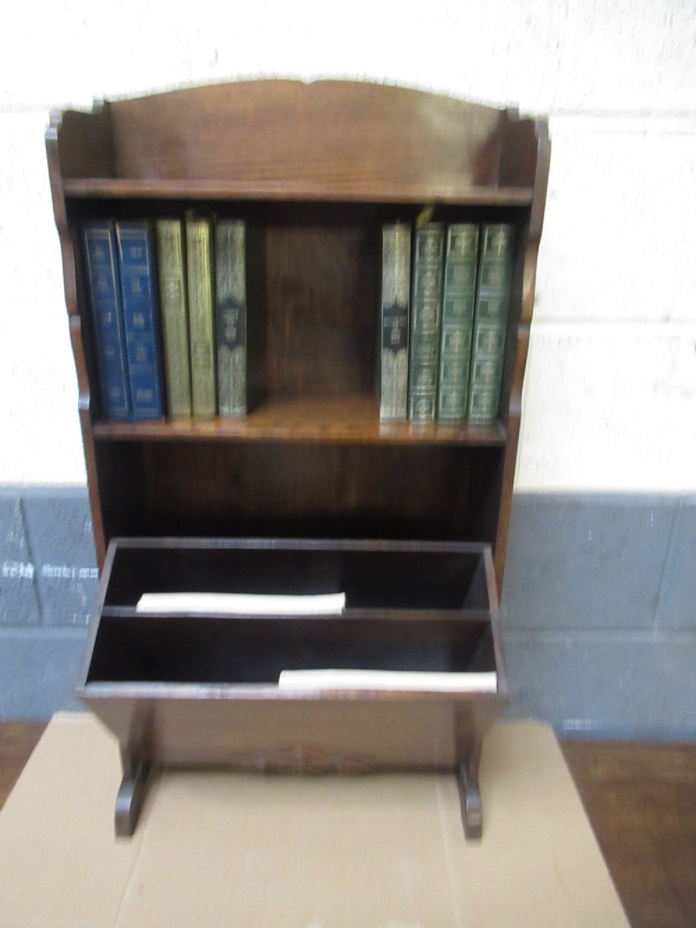 A 1930s dark oak freestanding book rack and magazine holder featuring open shelving above a partitioned lower trough with a carved shell motif. View IV