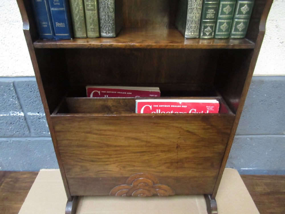A 1930s dark oak freestanding book rack and magazine holder featuring open shelving above a partitioned lower trough with a carved shell motif. View V