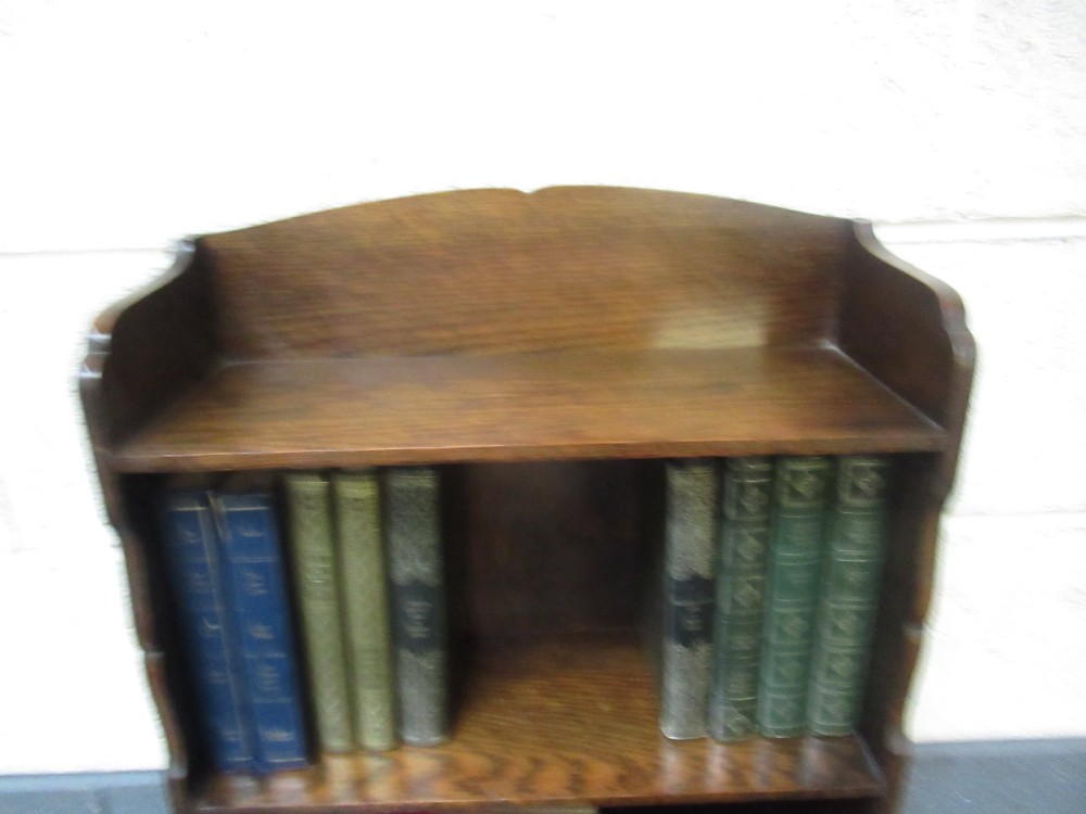 A 1930s dark oak freestanding book rack and magazine holder featuring open shelving above a partitioned lower trough with a carved shell motif. View VII