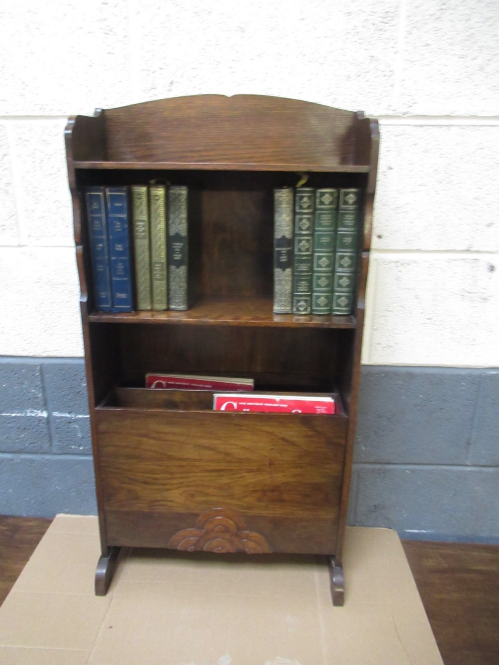A 1930s dark oak freestanding book rack and magazine holder featuring open shelving above a partitioned lower trough with a carved shell motif. View VIII