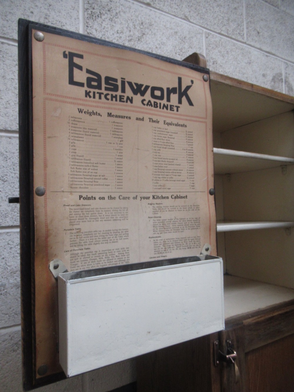 A freestanding 1920s solid oak kitchen cabinet featuring upper and lower panelled cupboards, drawers with glass knobs, and exposed copper hinges. View XI