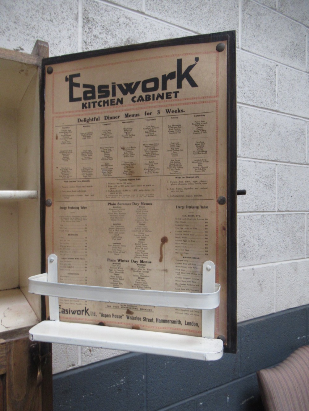 A freestanding 1920s solid oak kitchen cabinet featuring upper and lower panelled cupboards, drawers with glass knobs, and exposed copper hinges. View XIII