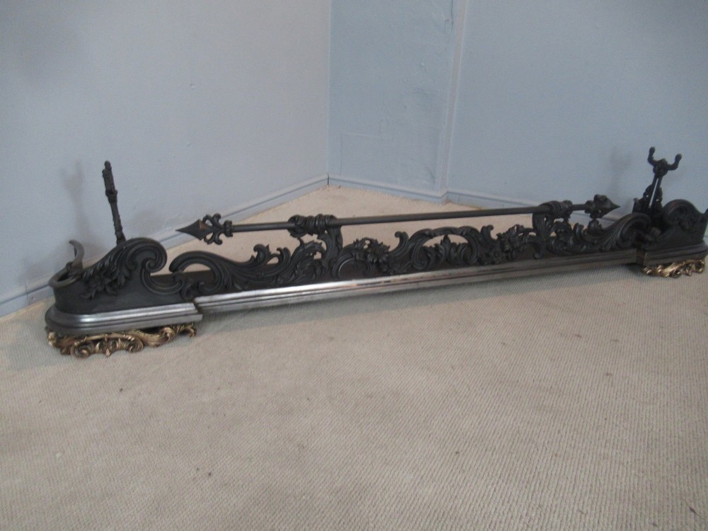 A nineteenth-century cast iron fire fender featuring detailed scrolling foliage ornament, a central spear-head rail, and brass feet.