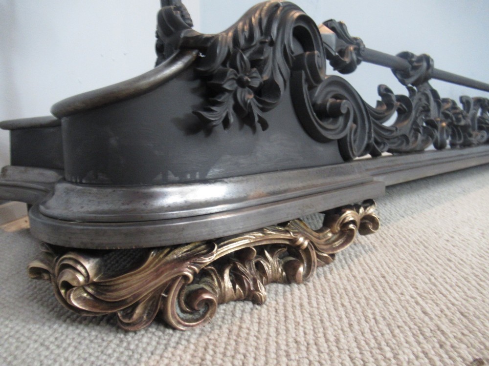 A nineteenth-century cast iron fire fender featuring detailed scrolling foliage ornament, a central spear-head rail, and brass feet. View II