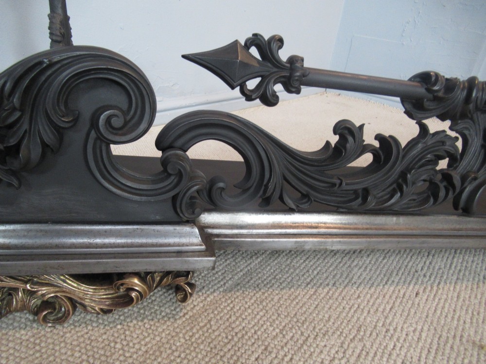 A nineteenth-century cast iron fire fender featuring detailed scrolling foliage ornament, a central spear-head rail, and brass feet. View III