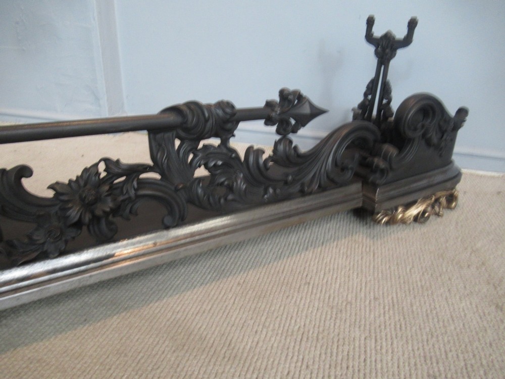 A nineteenth-century cast iron fire fender featuring detailed scrolling foliage ornament, a central spear-head rail, and brass feet. View IV